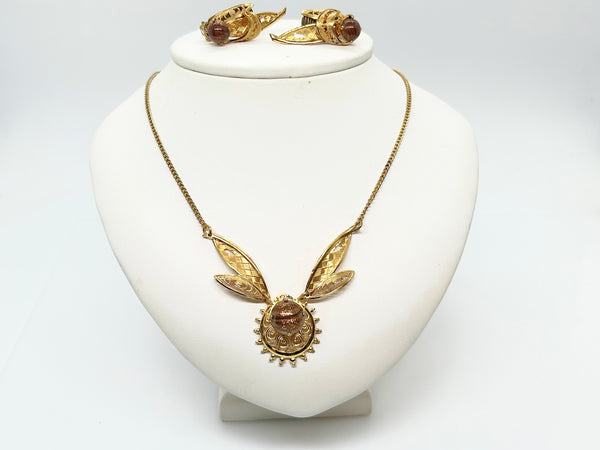 Vintage gold-tone filigree demi-parure jewelry set featuring a matching necklace and clip-on earrings, each showcasing an intricate textured leaf design and a central round, chatoyant brown art glass stone against a plain white background