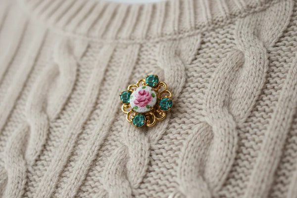 Take a closer look at this vintage gold-tone guilloche enamel rose scatter pin with blue rhinestones. The pin features a hand-painted pink rose on a white enamel center, surrounded by four aqua/turquoise blue glass rhinestones. 