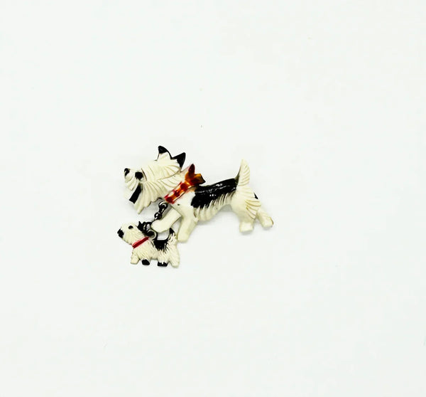 This is such an adorable pin. It is made of two black and white terrier dogs, one larger and the other smaller, puppy. The larger dog measure 1.25” across and wears a red, orange and white checked collar; the puppy wears a solid red collar and measures 1/2” across. 