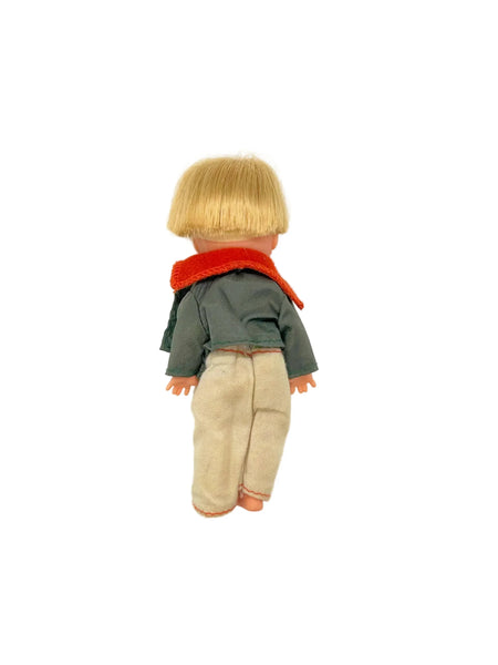 Vintage boy doll with blonde hair, green jacket, red scarf, and cream pants