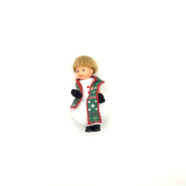 A vintage 2001 Mattel Barbie Kelly Club "Snowman Tommy" Christmas ornament doll. The small collectible figure has blonde hair, blue eyes, and a cheerful expression. It is dressed in a white snowman bodysuit accented with a green snowflake-patterned holiday vest with red trim and black mittens. Isolated on a solid white background