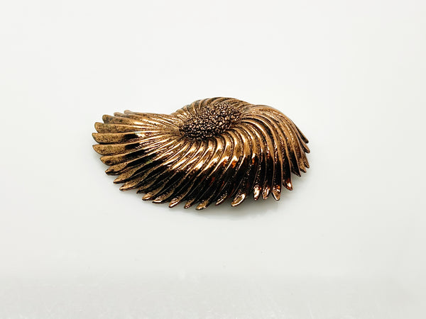 Vintage Tortolani copper-toned shell brooch featuring a textured, swirling modernist design reminiscent of a nautilus shell with a central cluster of dense, nugget-like details against a solid white background