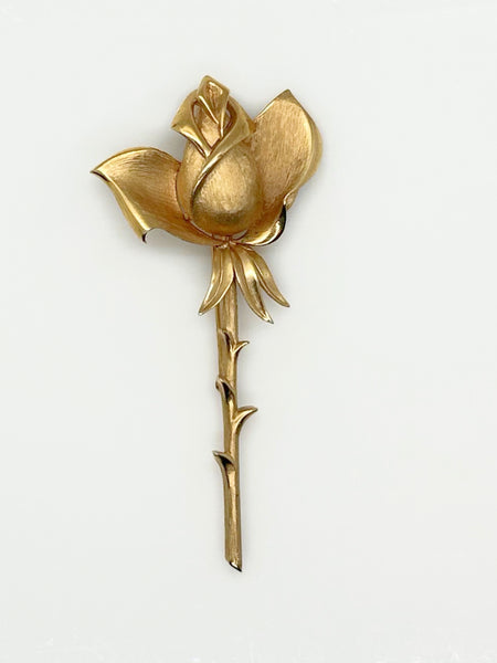 Vintage Crown Trifari gold-tone long-stem rose brooch featuring a detailed, textured matte rosebud on a thorny gold stem against a clean white background.