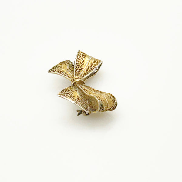 Side angle view of a vintage gold filigree bow brooch showcasing the dimensional openwork ribbon folds on a white background.