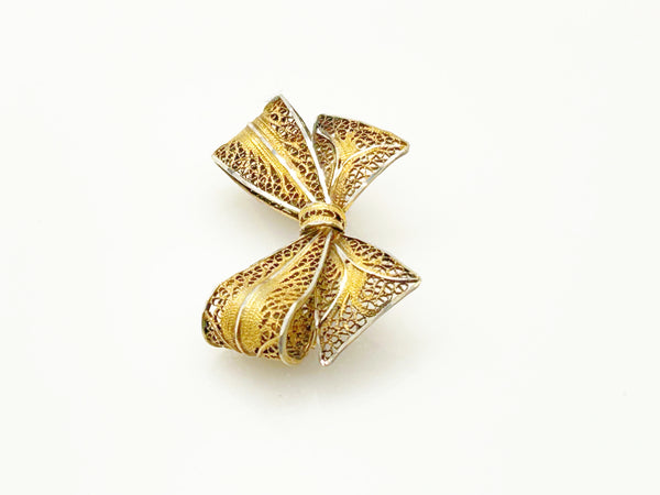 Side angle view of a vintage gold filigree bow brooch showcasing the dimensional openwork ribbon folds on a white background.