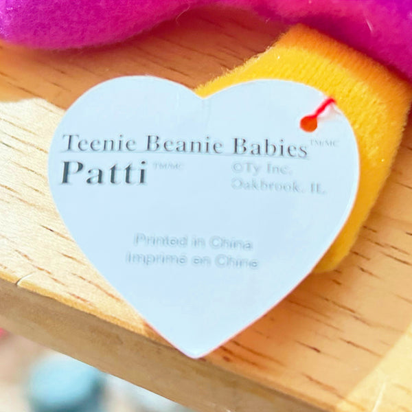 A close-up of a heart-shaped white paper tag attached to a plush toy, reading 'Teenie Beanie Babies Patti' with 'OTy Inc. Oakbrook, IL' and 'Printed in China' visible.