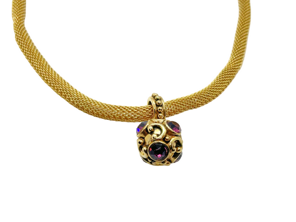 This 1990s pendant necklace features a meticulously crafted design with round purple faceted gemstones set in bezel-mounted antiqued gold metalwork. The ornamental pendant is suspended from a rounded mesh chain, measuring 16" secured with a toggle clasp.