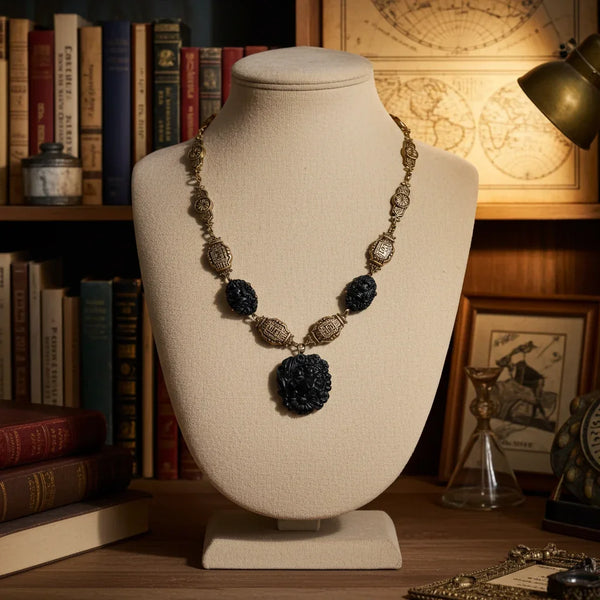An ornate necklace displayed on a cream fabric jewelry bust, set against a warm, vintage-themed background of bookshelves, a globe map, and a brass lamp.