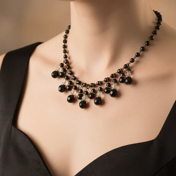 This wonderful vintage German bib necklace features black glass and clear beads in a choker or "Cleopatra fringe" style. These pieces are characterized by their intricate, cascading drop designs. 