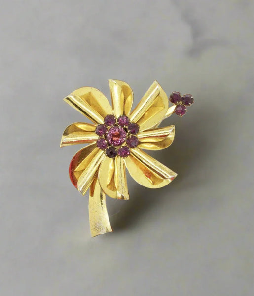 This is a an exemplary example of the floral pins made in sterling with a gold wash from the last century. A purple faceted stone is surrounded by smaller purple stones, and three more accent the top of a petal. 