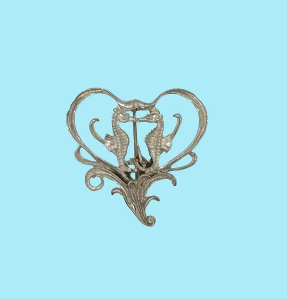 This unusual vintage open work brooch, meeting in a heart shaped frame, is sure to add a unique touch to any ensemble or collection. The detail and flourishes are lovely. The brooch measures 1.75" across at the widest area, and is in very good condition.